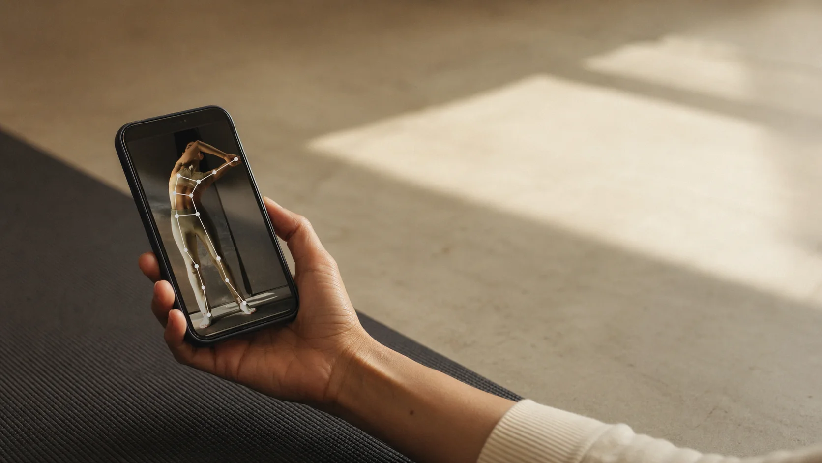 Hand holding a phone with a body tracking overlay on a yoga mat